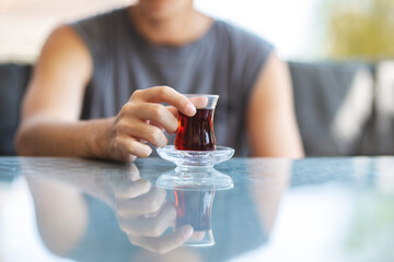 Close-up of man's hand holding glass of Turkish tea on reflection background table