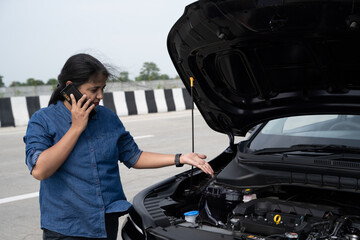 Young Indian woman standing by her car with the hood open, gazing at the damaged engine in frustration as she tries to figure out the problem 