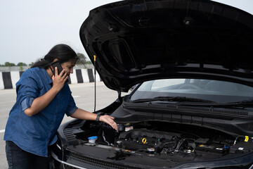 Young Indian woman standing by her car with the hood open, gazing at the damaged engine in frustration as she tries to figure out the problem 