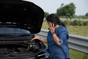 Young Indian woman standing by her car with the hood open, gazing at the damaged engine in frustration as she tries to figure out the problem 