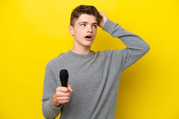 Singer Teenager man picking up a microphone isolated on yellow background having doubts and with...
