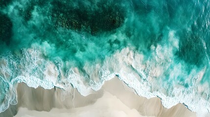 Obraz premium Aerial view of a vibrant turquoise ocean meeting a sandy beach, showcasing foamy waves and clear waters.
