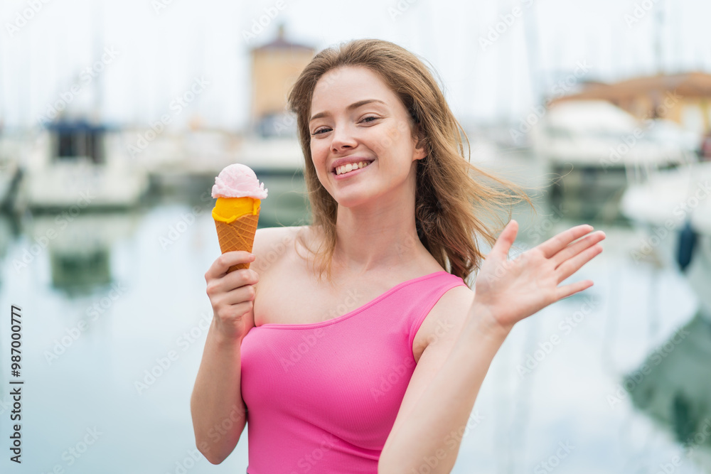 Canvas Prints Young redhead woman with a cornet ice cream at outdoors saluting with hand with happy expression