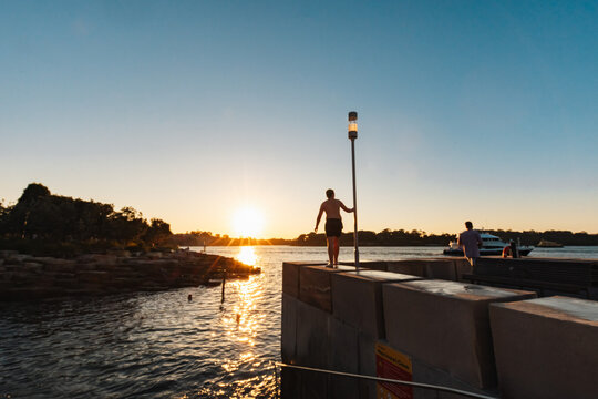 Teenage boy standing on ledge by water in bright setting sun