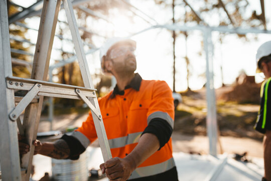 Construction worker holding a steel ladder while looking up.