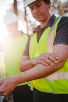 Construction worker on a blurry background rubbing sunscreen lotion on his arm.