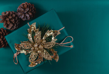 Christmas gift box with gold flower decoration, pine cones on green background