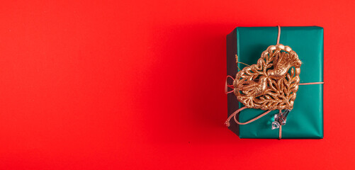 Banner green Christmas gift box with gold heart decoration on red background