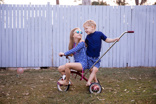 young kids grinning at each other on the back of a trike