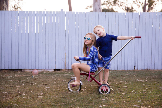 two young kids playing on a trike in the backyard