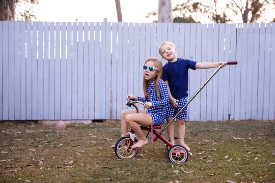 sister sitting on a trike while her brother stands on the back