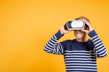 Portrait Asian smiling old man holding in a virtual reality glasses headset studio shot isolated yellow background, Excited happy senior man pensioner using VR play simulation game
