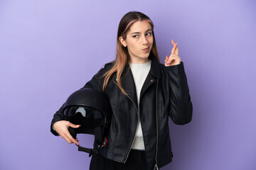 Young caucasian woman holding a motorcycle helmet isolated on purple background with fingers crossing and wishing the best