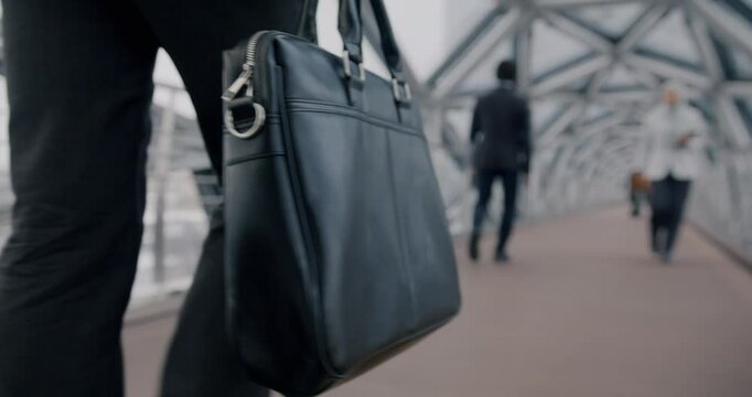 Close-up of briefcase moving in businessman's hand while person walking in futuristic glass corridor in office building in daylight
