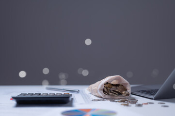 Close-up view of desktop featuring coins spilling from bag, alongside calculator and financial...
