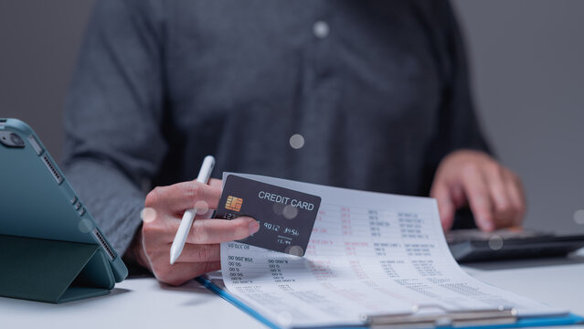 Person reviews financial documents while holding credit card, importance of careful financial management and planning for personal budgeting and expenditures