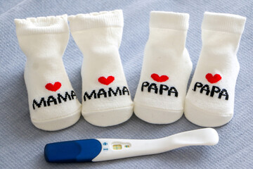 Positive pregnancy test alongside cute little pairs of newborn baby socks with love heart mama and papa design. Preparation and anticipation of pregnancy, birth and parenthood concept.