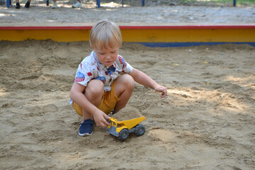 Cute toddler boy playing in sand on outdoor playground. Beautiful baby having fun on sunny warm summer day. High quality photo
