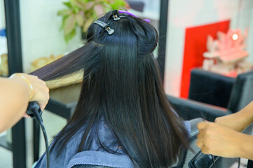 Two hairdressers using hair straighteners Straightening the hair of a female customer to make it beautifully straight in a beauty salon, hair care in Thailand