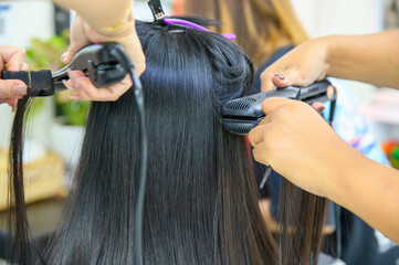 Two hairdressers using hair straighteners Straightening the hair of a female customer to make it beautifully straight in a beauty salon, hair care in Thailand