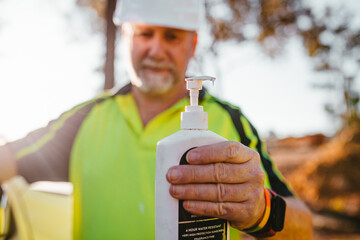 Construction worker on a blurry background holding a pump bottle.
