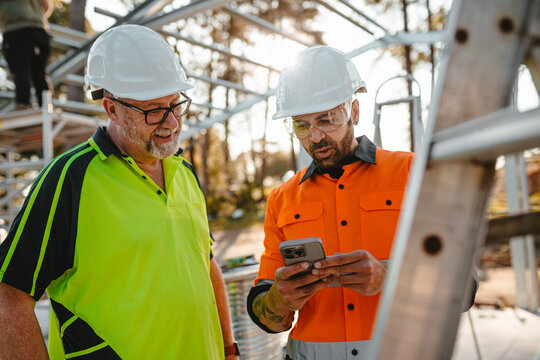 Two men wearing safety gears on the site with one holding a mobile device.