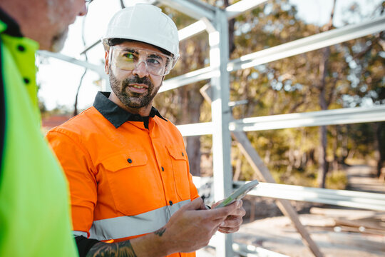 Two men wearing safety gears on the site with one holding a mobile device.