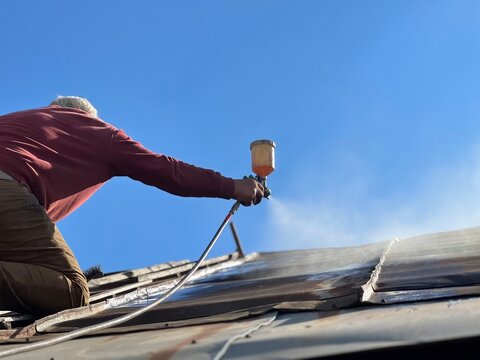 man working on roof, treating rusty old roof before painting on sunny day