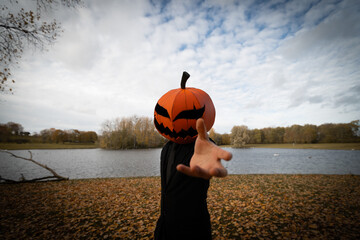 A whimsical figure with a pumpkin head standing amidst a colorful autumn landscape, surrounded by...