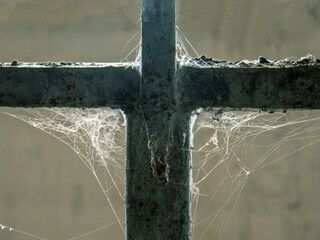 White threads of spider web on right angle dirty metal construction cross close up view