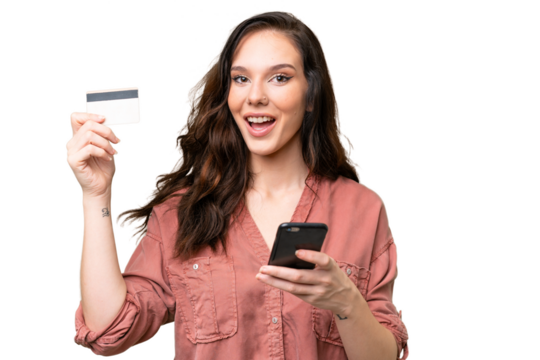 Young caucasian woman over isolated background buying with the mobile and holding a credit card with surprised expression