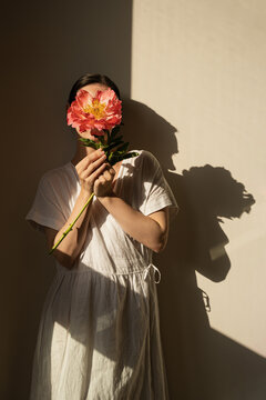 Minimalist Scene. Woman in White Dress, Flower-Covered Face, Gentle Shadows, Natural Lighting