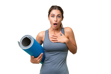 Pretty Young Uruguayan sport woman going to yoga classes while holding a mat over isolated background surprised and shocked while looking right