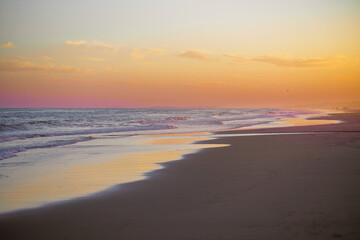 Golden sunset reflects on the tranquil shoreline as waves gently meet the sand.
