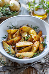 Baked potato wedges seasoned rosemary, garlic and olive oil served in white ceramic bowl, close up view