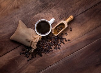 A cup of coffee, coffee beans, and a wooden scoop on a wooden table.
