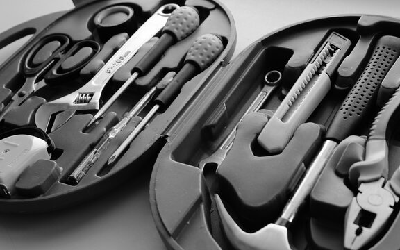 Hammer, pliers, mounting knife, scissors, electrical tape, voltage tester, measure roller and screwdrivers in a toolbox grayscale stock photo