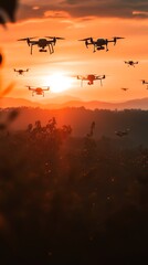 Several drones fly in formation against a bright orange sunset over a mountain range and trees.