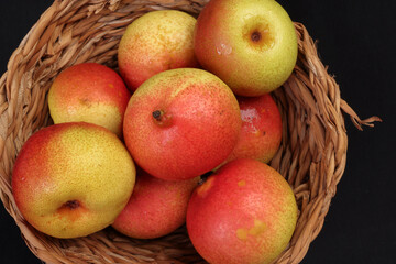 Green yellow red ripe mini pear sweet juicy in basket on wooden table dark background