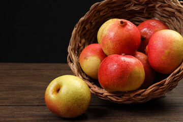 Green yellow red ripe mini pear sweet juicy in basket on wooden table dark background