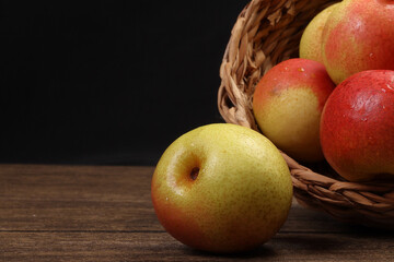 Green yellow red ripe mini pear sweet juicy in basket on wooden table dark background