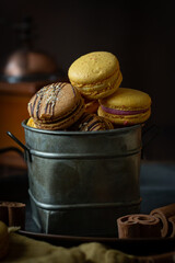 French macaroons of different colours yellow, orange, brown with pumpkins on dark background 