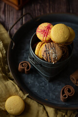 French macaroons of different colours yellow, orange, brown with pumpkins on dark background 