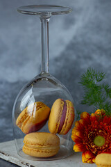 French macaroons of yellow colour in a wine glass with orange red flowers on blue grey  background 