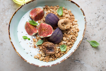 Bowl of granola with fresh and dried fig fruits and greek yogurt, horizontal shot on a beige granite surface, middle close-up