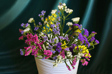 Bouquet of multicolored flowers in a vase (Limonium sinuatum, Statice sinuata) on a green background