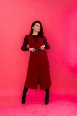 A woman in a red dress poses for the camera. She is wearing black boots and a belt.