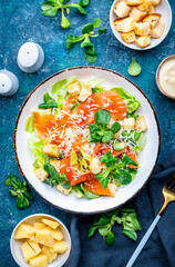 Foodie food caesar salad with salmon, iceberg  lettuce, croutons, grated parmesan with dressing. Blue background, top view
