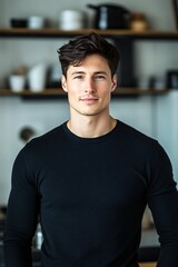 Fototapeta premium Young Man in Black Sweater Standing in Modern Kitchen with Neutral Expression