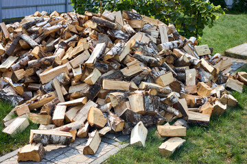 Birch chopped firewood woodpile over grass near fence.